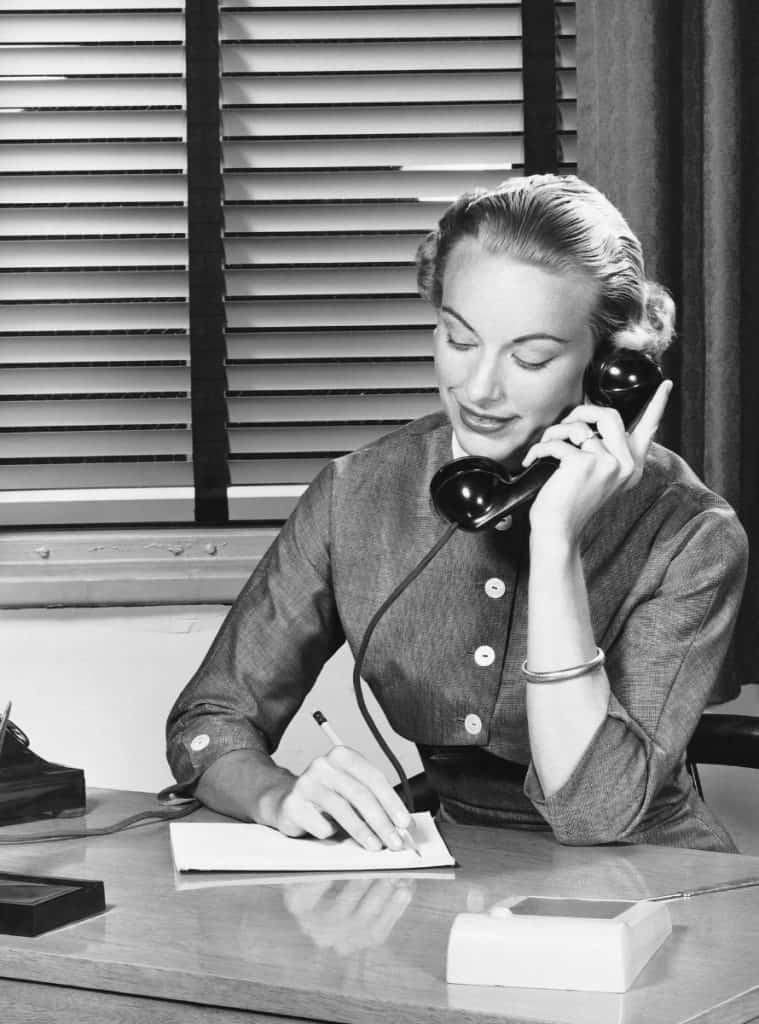A black and white photo of a woman answering an old-fashioned phone
