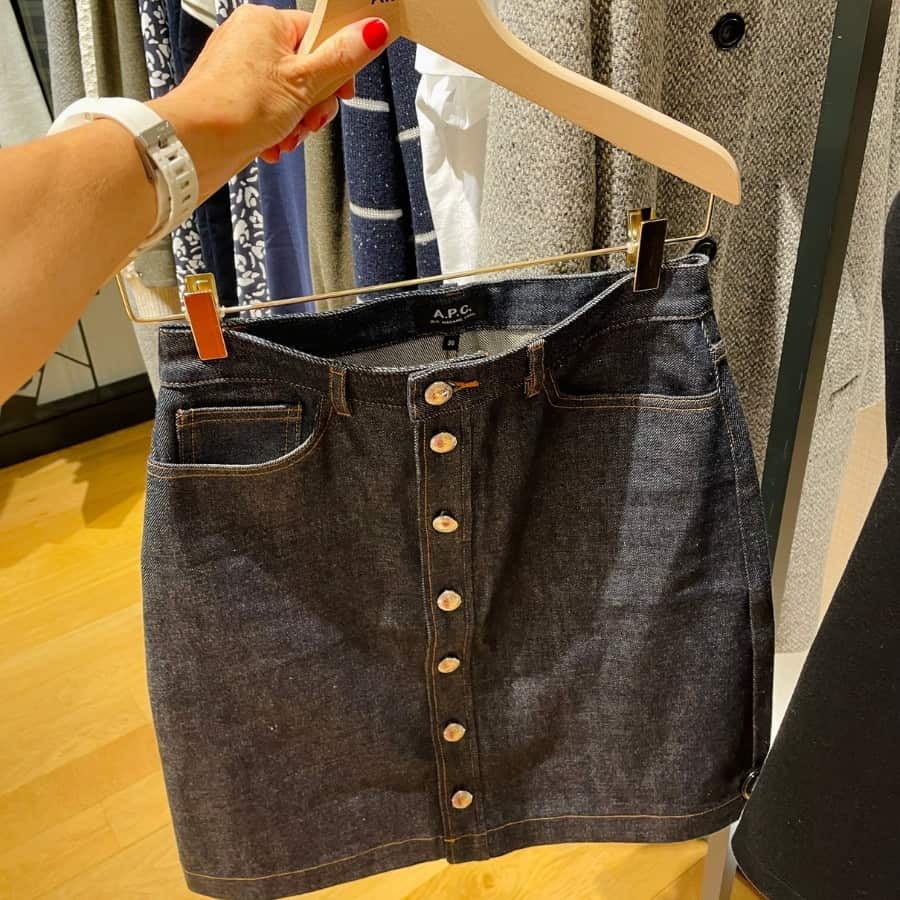 A woman's hand holds up a denim skirt by A.P.C. a French clothing brand