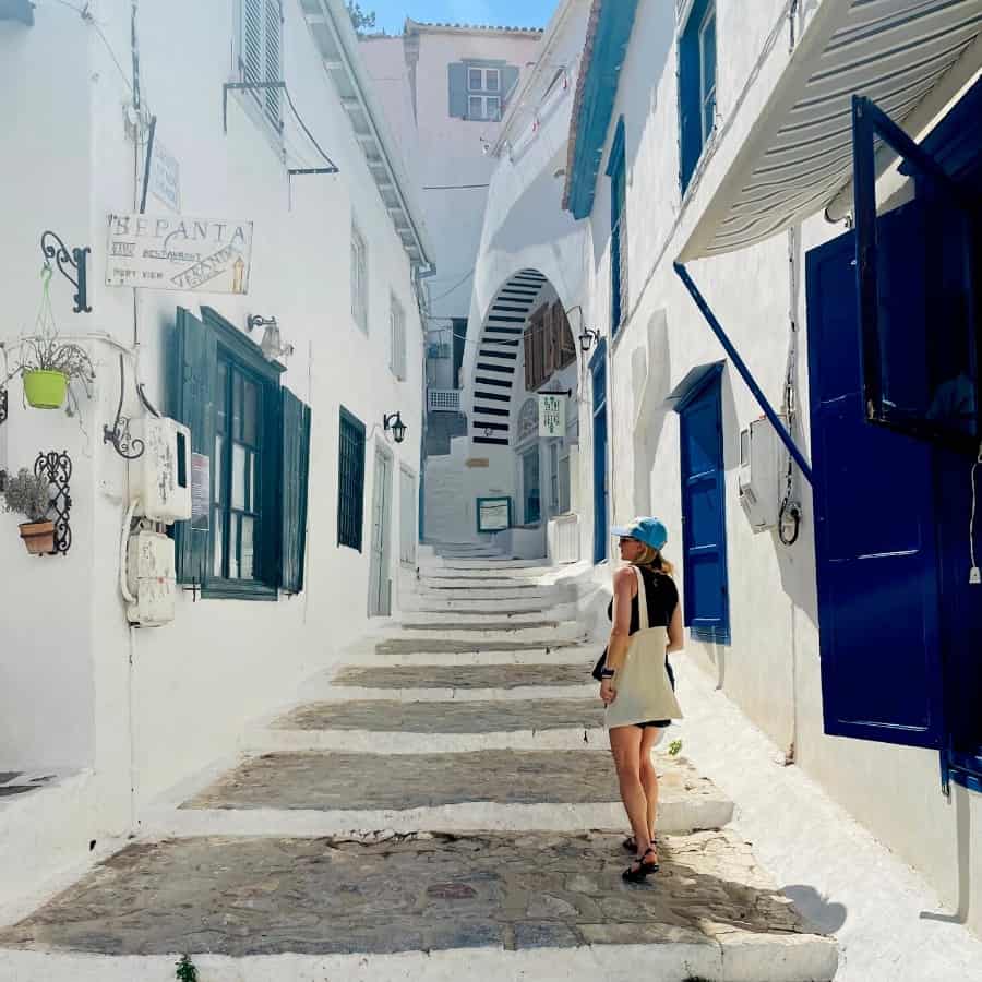 Ashley Blake, founder of Traverse Journeys walks up white washed steps in a narrow alley in Hydra Greece