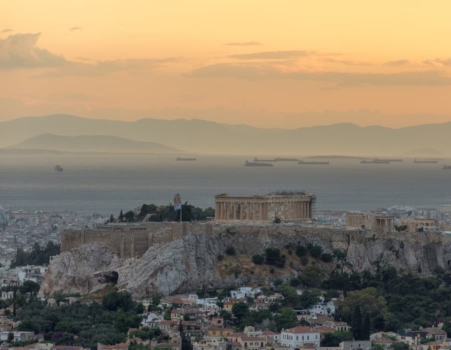 A broad view of Athens Greece with the Acropolis on a hill and the Aegean Sea visible beyond the city