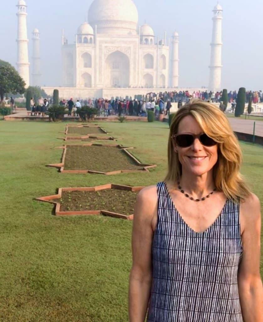 A woman stands in front of the Taj Mahal in India. She's wearing sunglasses and a striped dress.