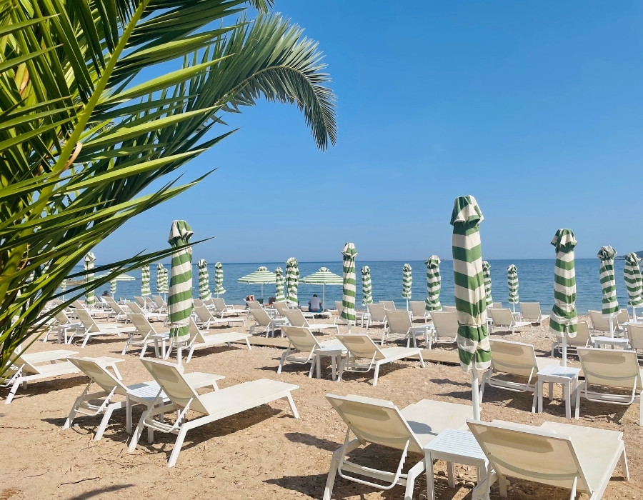 On the island of Spetses in Greece, a beach club has rows of white lounge chairs with green and white striped umbrellas