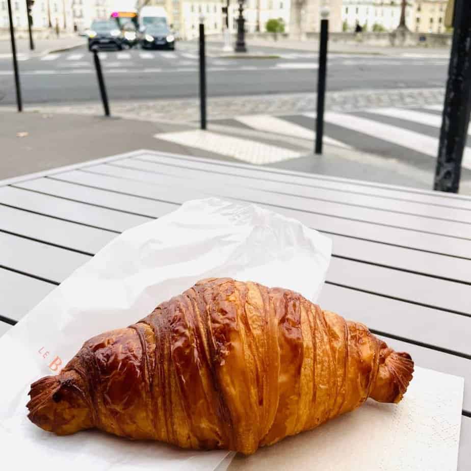 A butter croissant sits on a plate in Paris