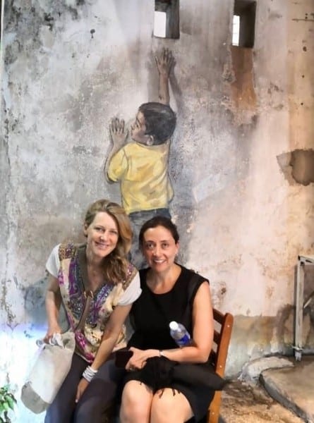 Two women sit on a chair underneath a mural titled Boy On A Chair in Penang