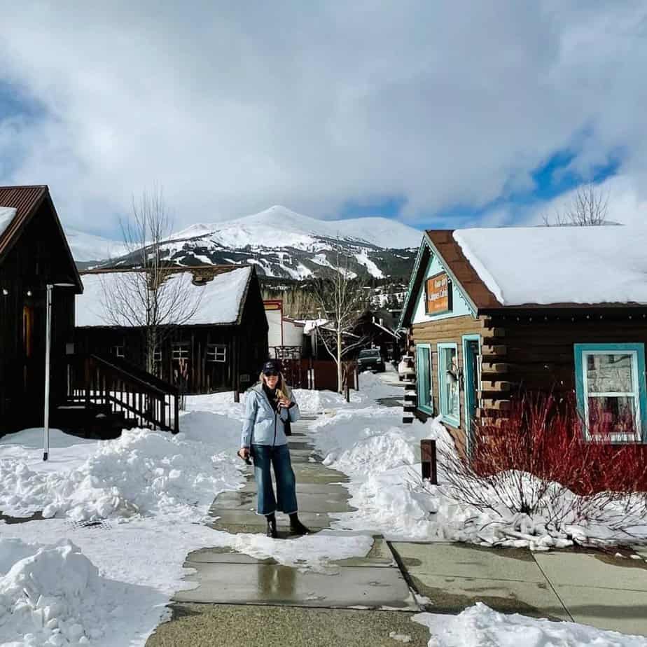 Susan Heinrich stands in the historic town of Breckenridge Colorado with as view of the ski mountain in the distance.
