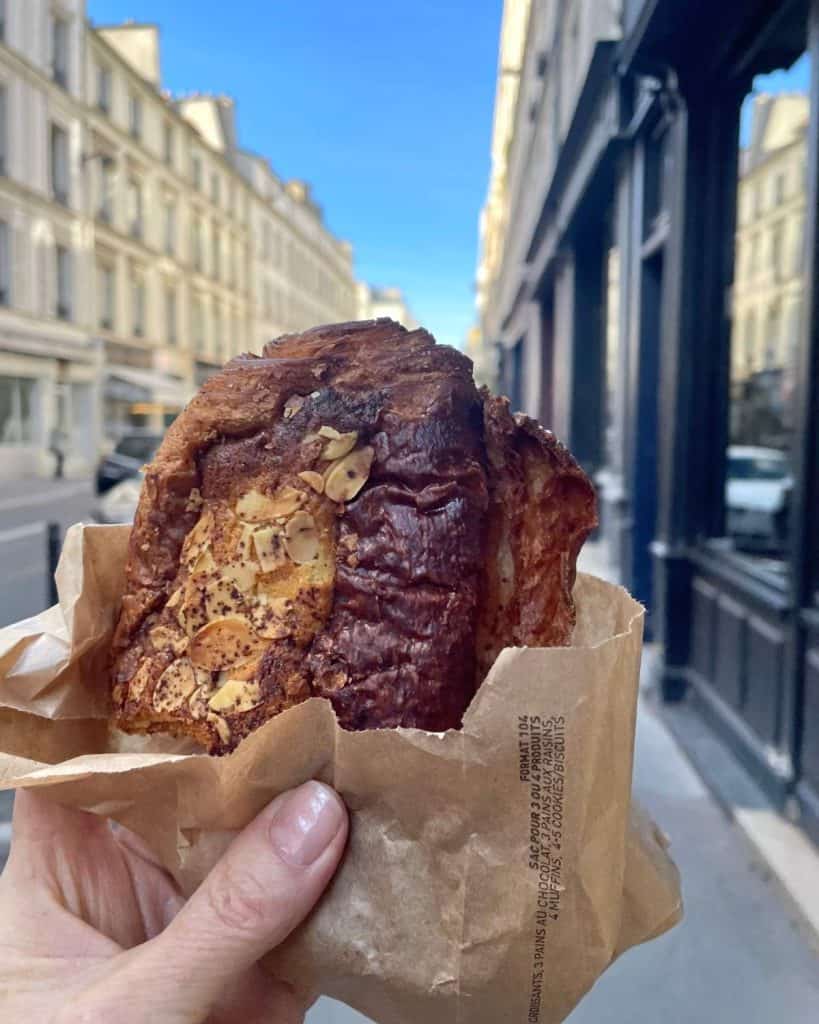 A hand holds out an almond croissant on a Paris street.