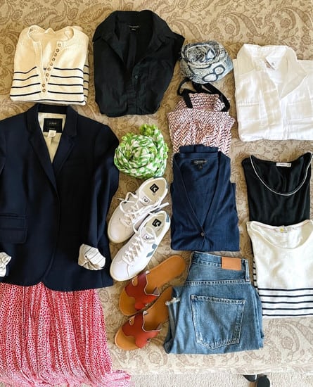 A capsule wardrobe for spring starts with a neutral palette of navy and white. Pictured are a flat lay of navy blazer, denim jeans, blue and white scarf, white shirt, navy cotton cardigan sweater, striped sweater and striped mariniere tee shirt. And colorful items include a pink shirt, pink patterned dress and green scarf