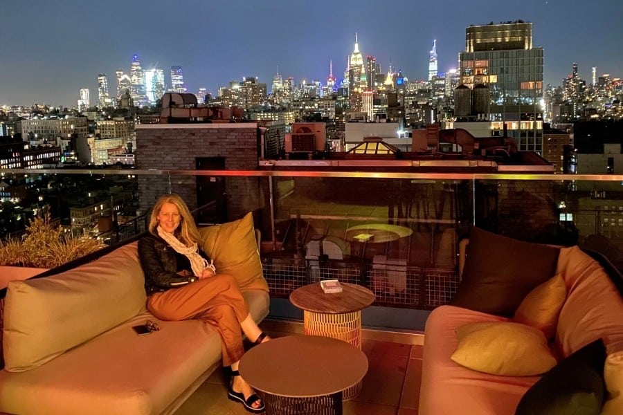 Susan Heinrich sits on a rooftop lounge in New York City withe the city and buildings beyond