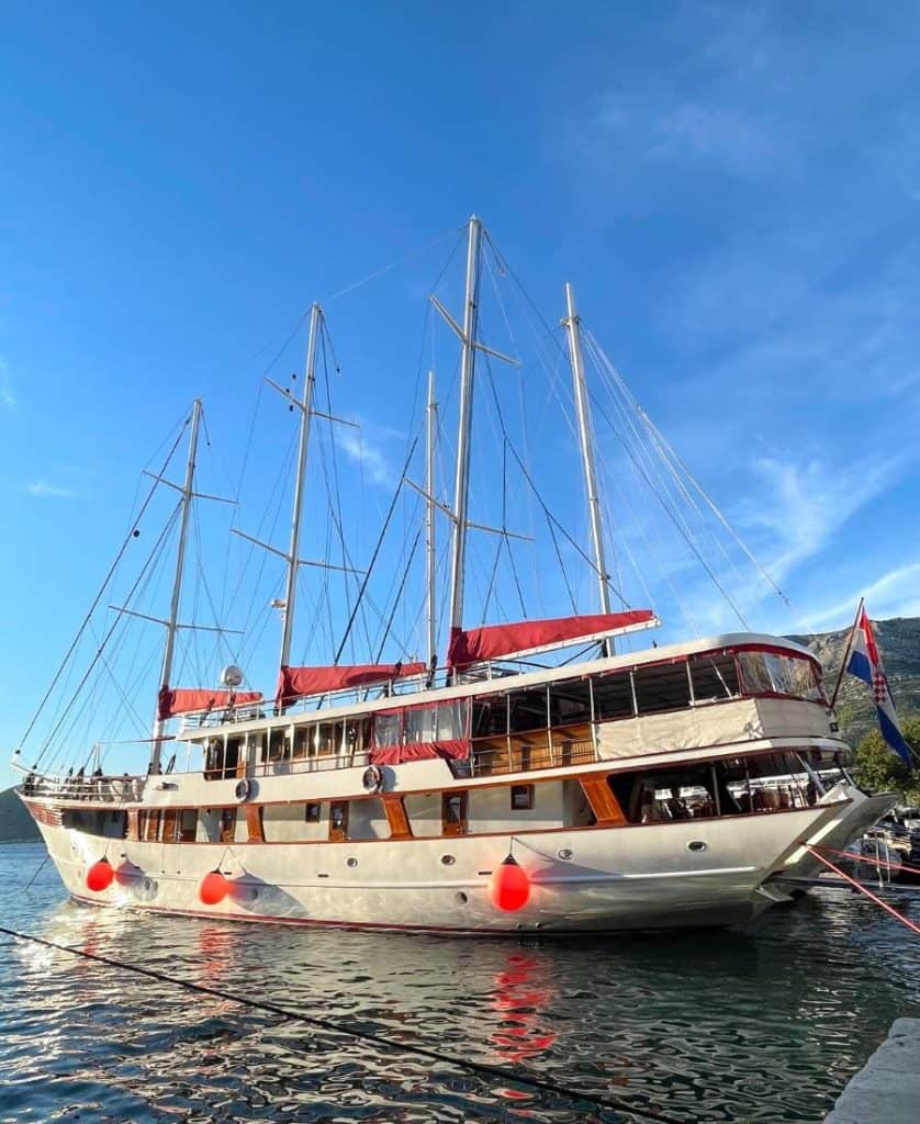 A white and red sailing yacht is moored at sea with four masts visible. Sails are not raised.