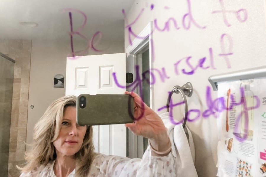 A woman faces a mirror with the words Be Kind to Yourself Today"