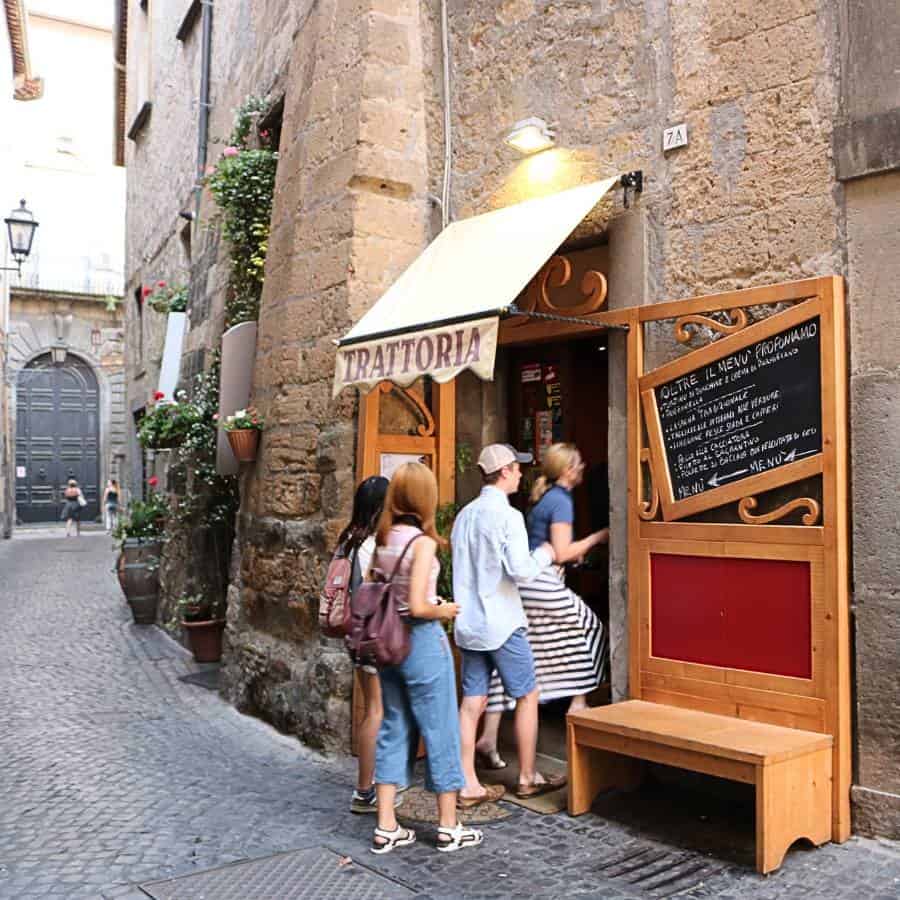 Several people are walking through a door into a trattoria on a cobblestone laneway in Orvieto.
