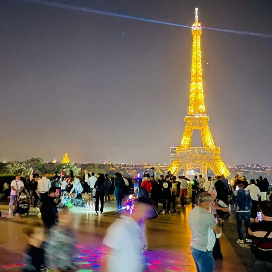 A view of the Eiffel Tower from the Trocadero in Paris with lots of people, lights and activity happening