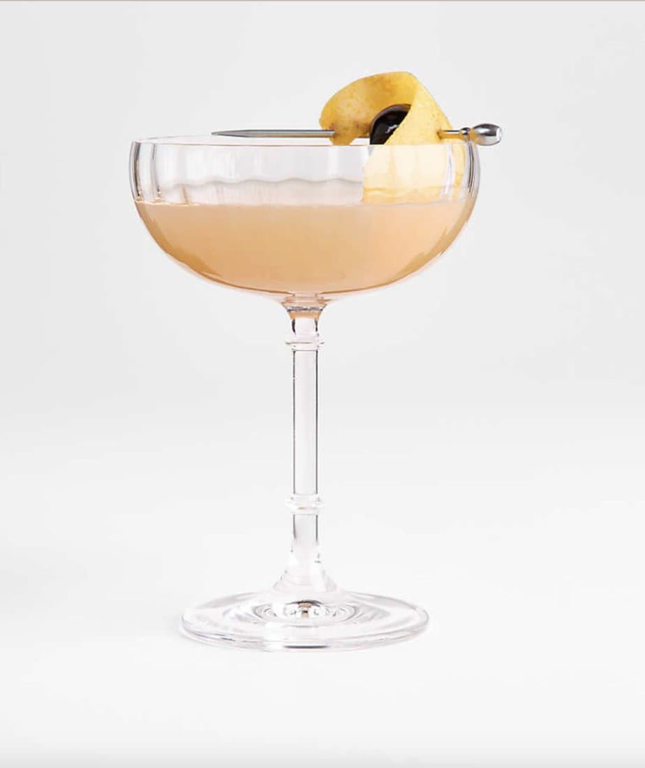 A French coupe glass is filled with a peach liquid and pretty lemon garnish