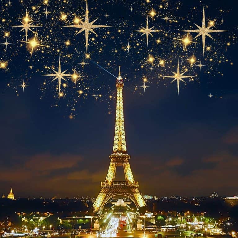 The Eiffel Tower is pictured against a dark night sky. Golden starbursts are set in the sky above it. A little of Paris is visible next to it.