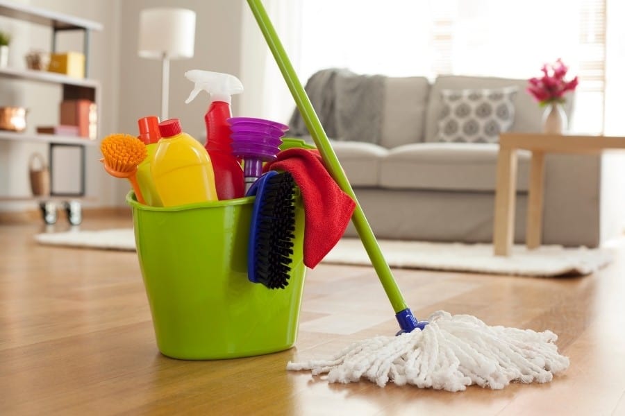 A bucket with colourful cleanig products on the floor of a living room