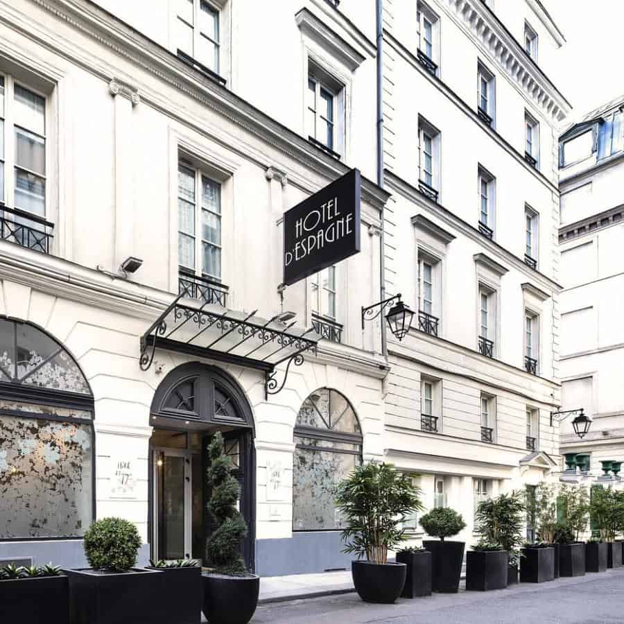 The 4-story exterior of Paris hotel is white with black accents and a row of potted plants in large black planters outside of the entrance.