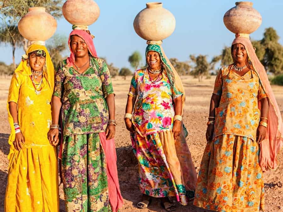 Indian women in colourful saris carry water jugs on their heads