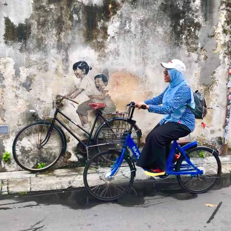Kids on a Bicycle street art with a cyclist riding past, in Penang