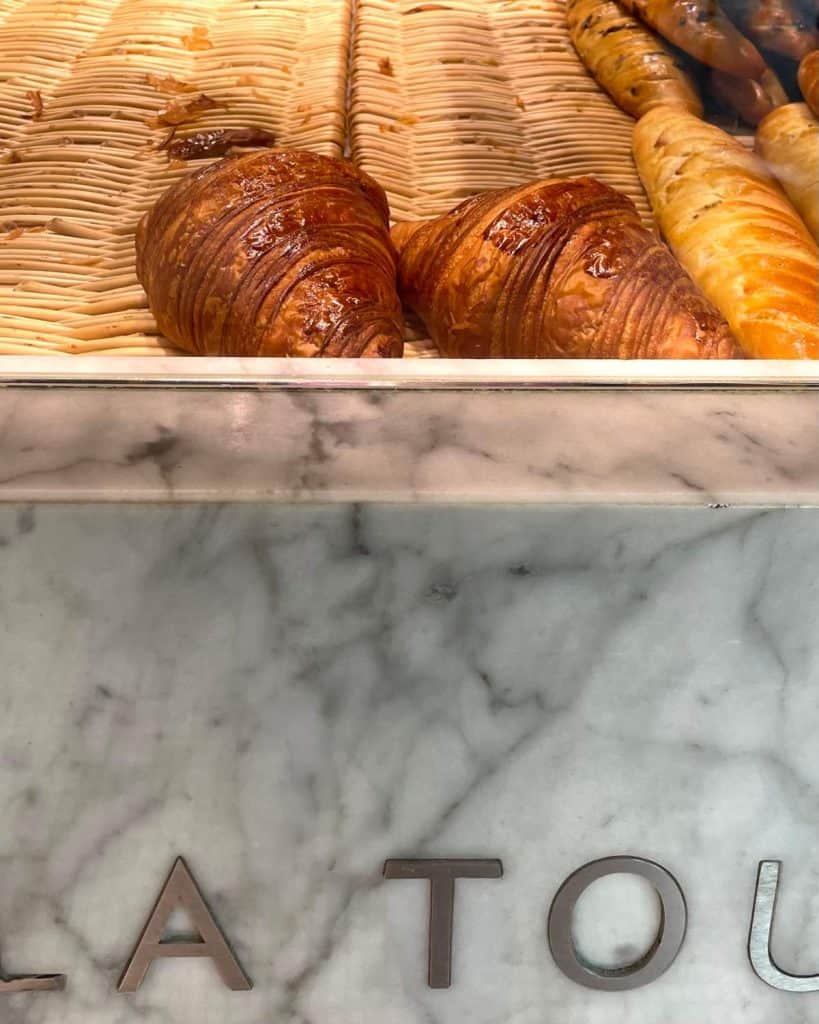 Two butter croissants remain in a woven basket above a marble counter.