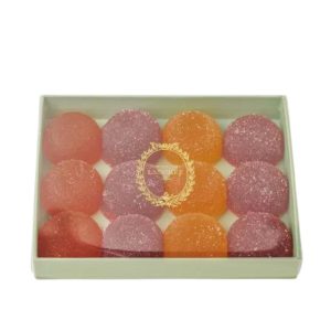 A package of 12 Laudurée Fruits de Pates, French fruit jellies from Paris.Three colors are shown, pink, purple and orange.The box has a clear lid with the Laudurée logo.