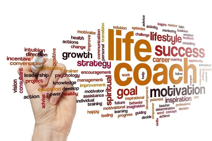 A hand writes on a whiteboard with motivational words surrounding larger text that says "life coach"