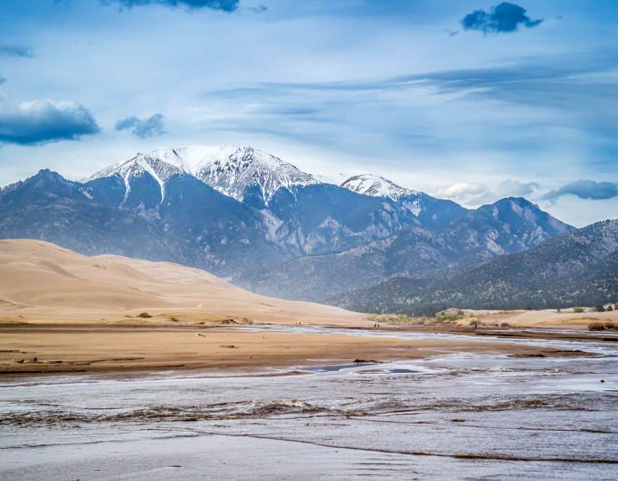 The water of Medano Creek in spring at Grand Sand Dunes National Park. Rolling sand dunes and the Sangre de Cristo Mountains are pictured beyond.