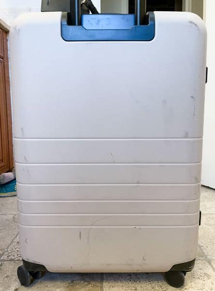 The Monos Medium checked bag in desert taupe, a light beige, covered in dark scuffs