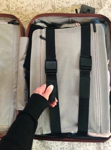 A hand pulls on a strap inside of a carry on bag to compress a fabric panel and the contents underneath