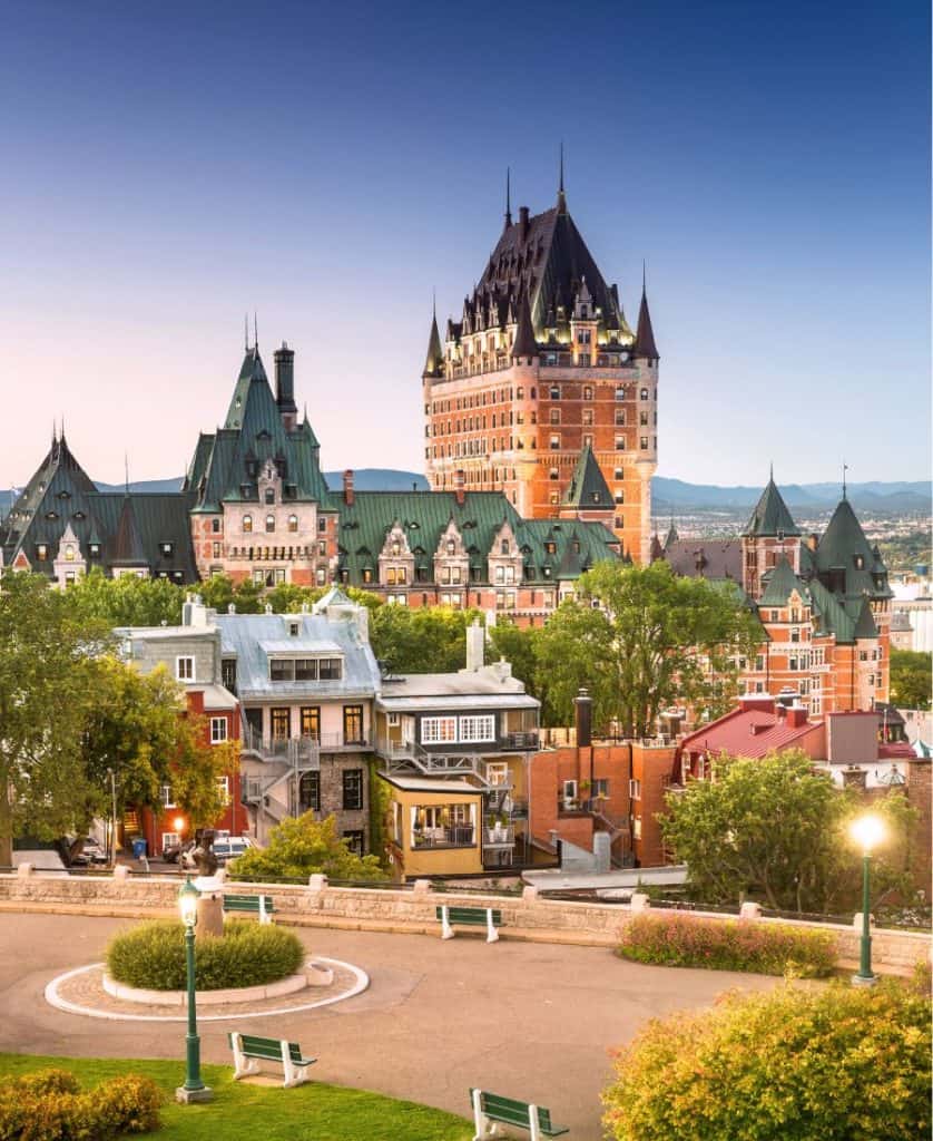 Rooftops of historic buildings in Old Quebec are pictured against a blue and pink sky at dusk. A park is pictured in the foreground.