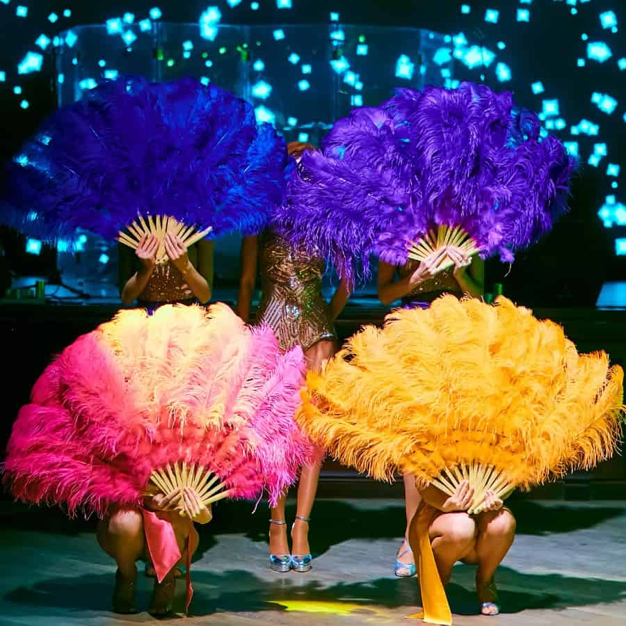 Four Paris cabaret dancers are on a stage with brightly colored fans of feathers covering their faces.