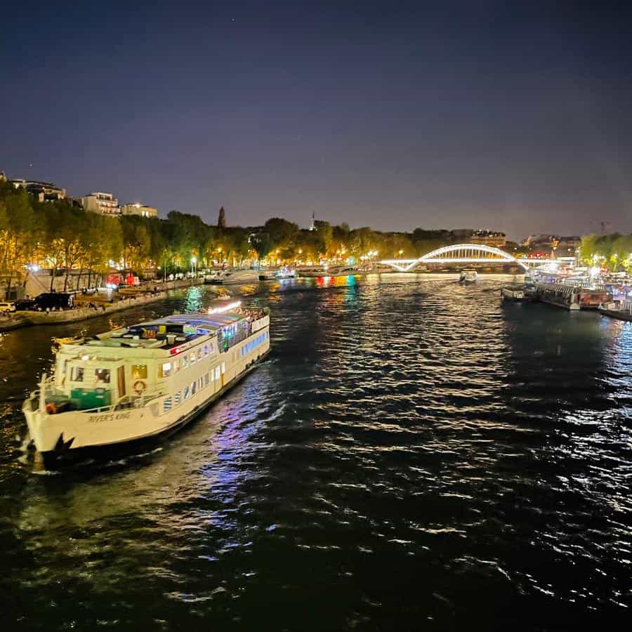 A boat moves along the seine in Paris at nighttime with a bridge lit up beyond