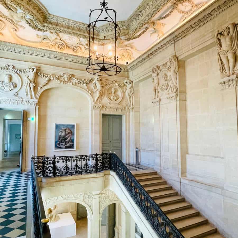 The interior stairs of the Picasso Museum are pictured surrounded by the beautiful architecture of the Hotel Salé, the historic building that houses the museum. A Paris hidden gem found in the Marais area.