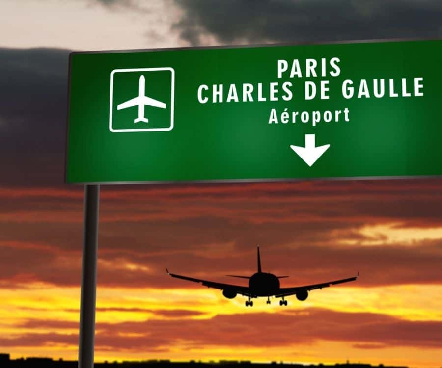 A plane flies beyond a sign to the Paris Charles de Gaulle airport
