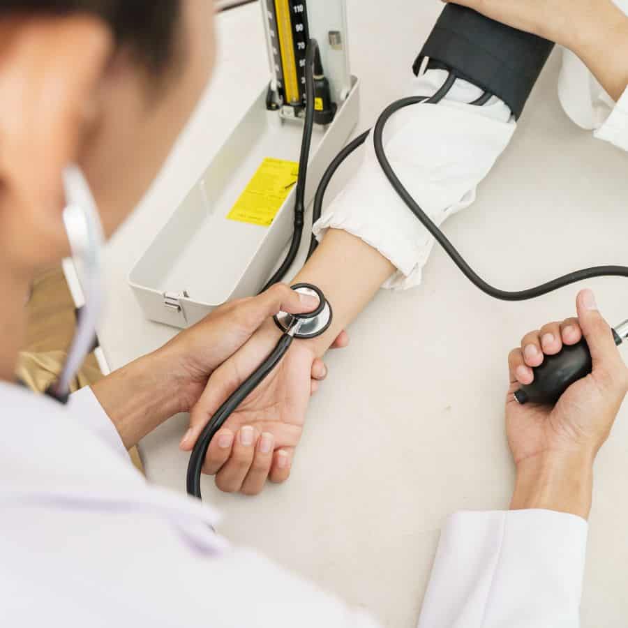 A woman's blood pressure is taken in a doctor's office. Only her arm is visible, along with a doctor holding her wrist and a stethoscope