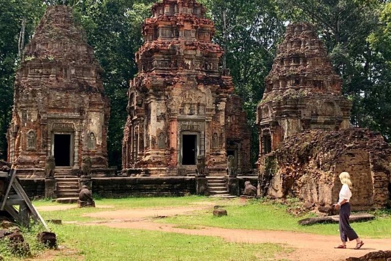 Susan Heinrich exploring the Preah Ko temple in Siem Reap Cambodia. She is pictured walking in profile in front of three temples that date to the 9th century.