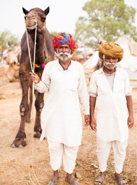 Two men walk with a camel during the Pushkar Camel Fair in India
