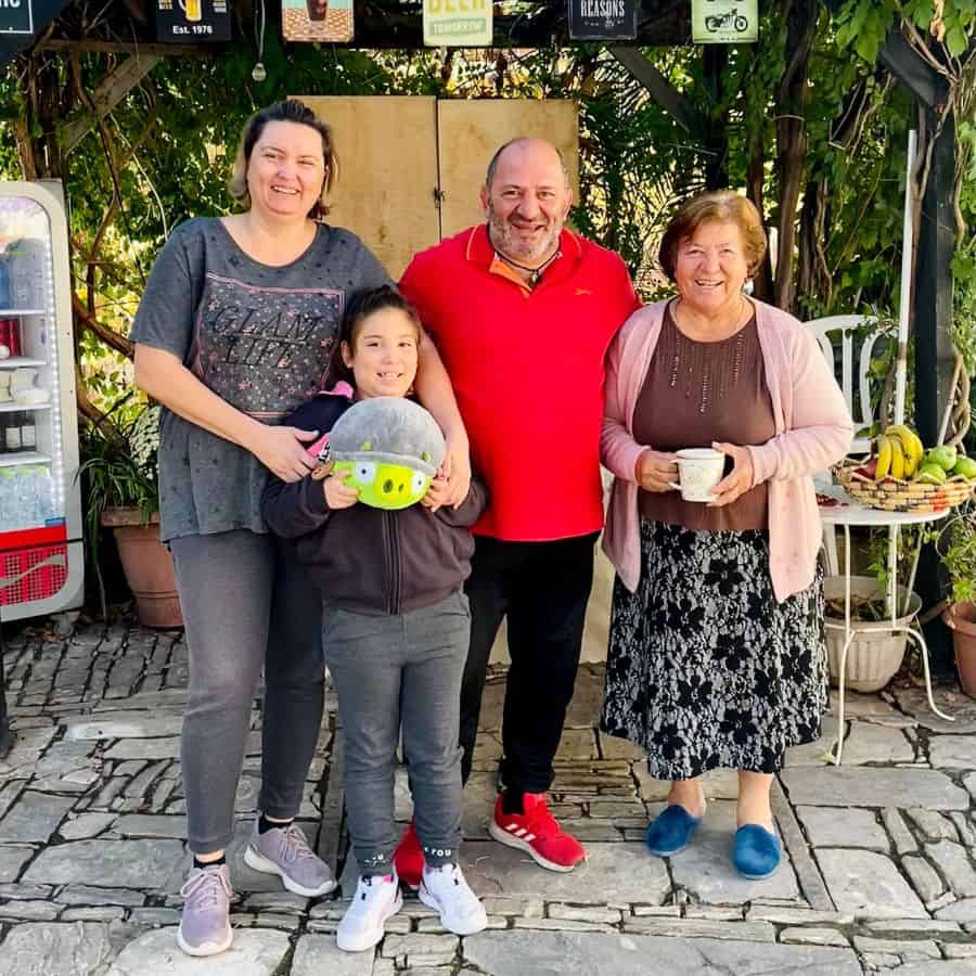A family of four stands in a taverna in Cyprus. They are smiling for the camera. Left to right they are the mother, daughter, father and grandmother.