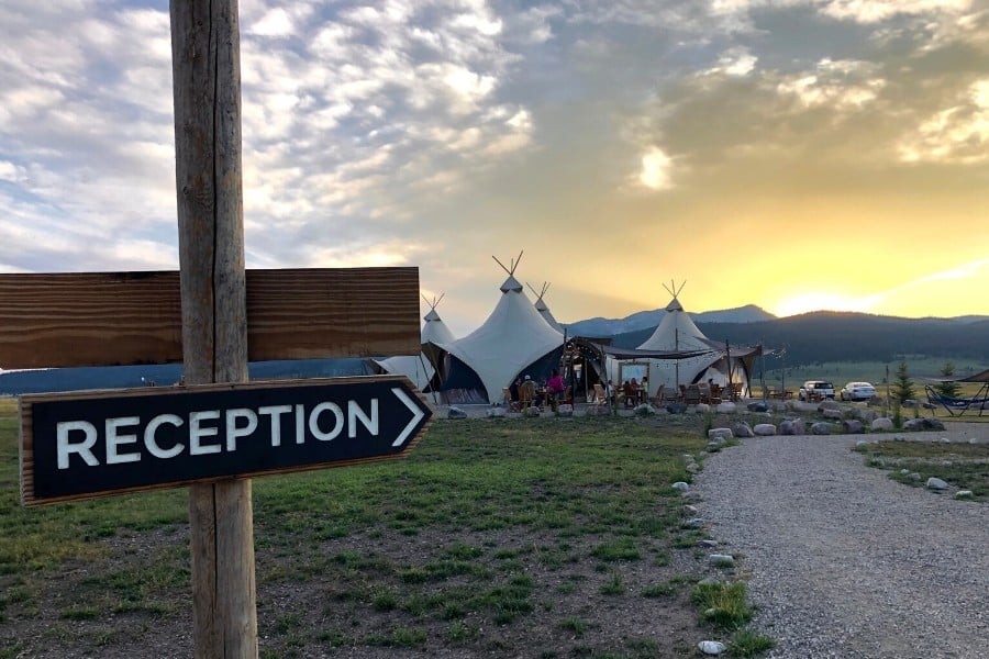 A reception sign points down a path toward a group of glamping tents at Under Canvas Yellowstone