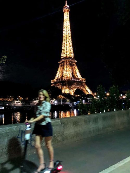 Susan Heinrich riding a scooter past the Eiffel Tower at night