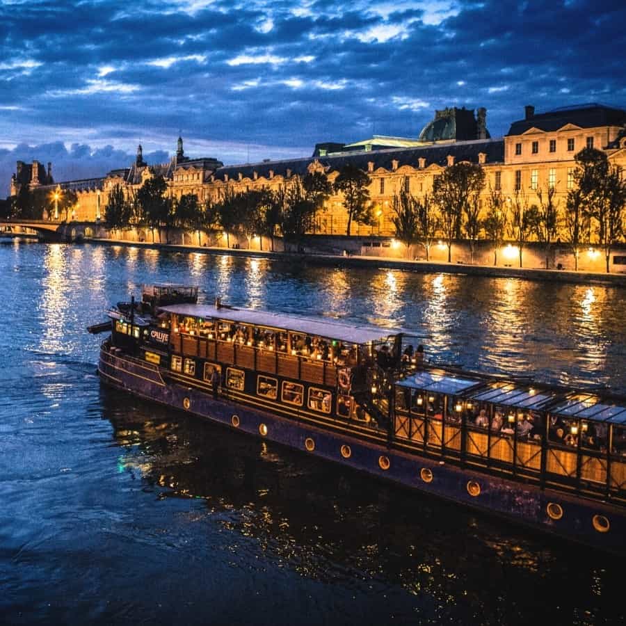 A boat travels along Paris's Seine River at night, with buildings lit up next to the river