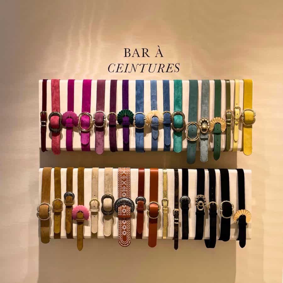 A wall display of about three dozen belts made of suede and leather and in a variety of colors, including purple, pink and yellow.