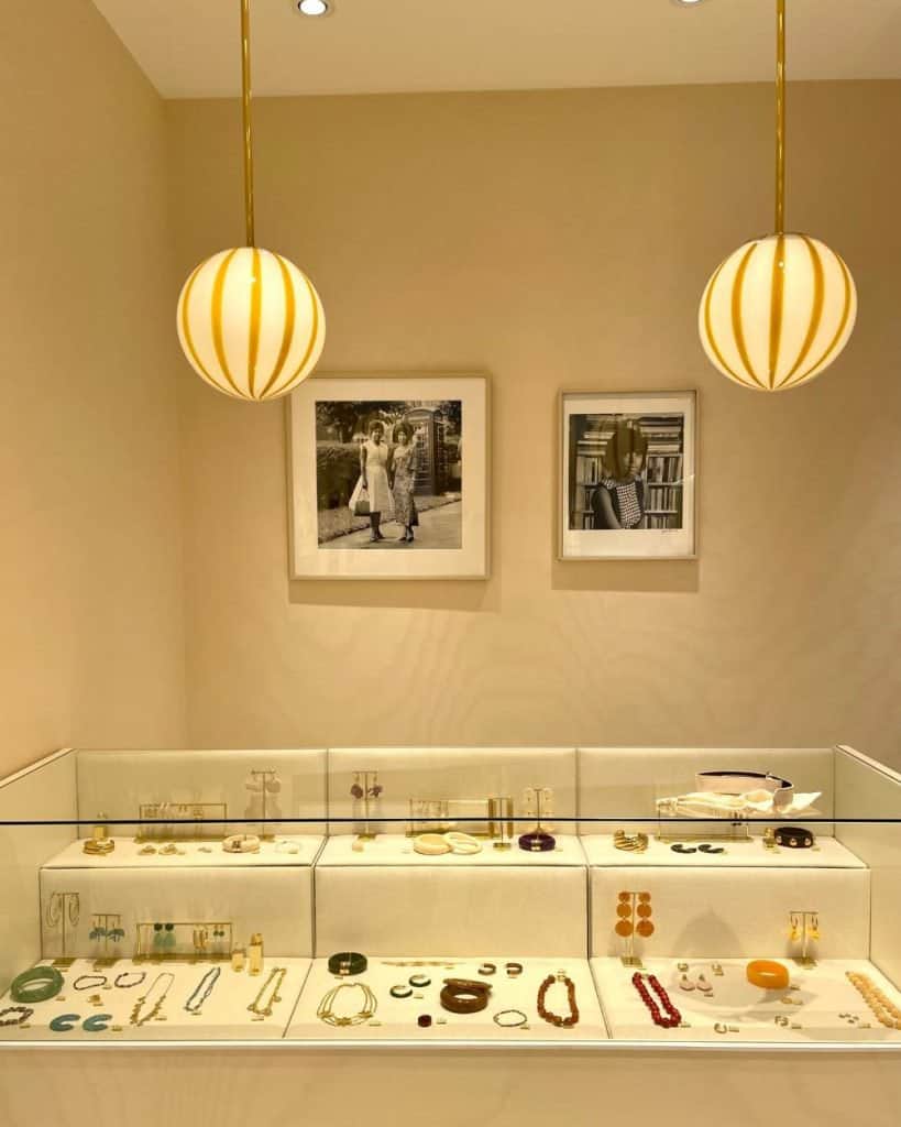 A display case of jewelry at a Paris Sézane store with two globe-shaped lights hanging over it and some framed art on the wall.