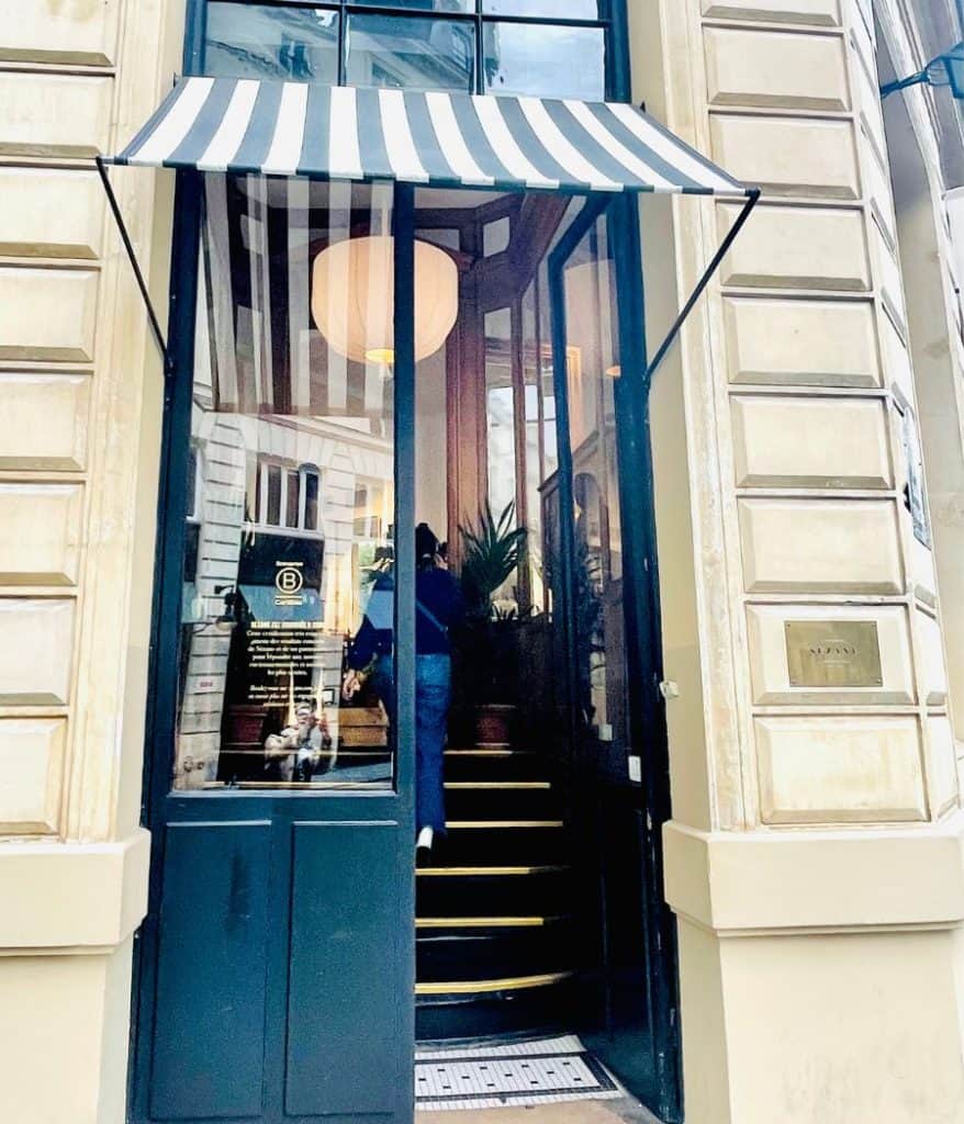 The entrance to a Sézane clothing store in Paris. The door is blue and a blue and white-striped awning hangs above it.