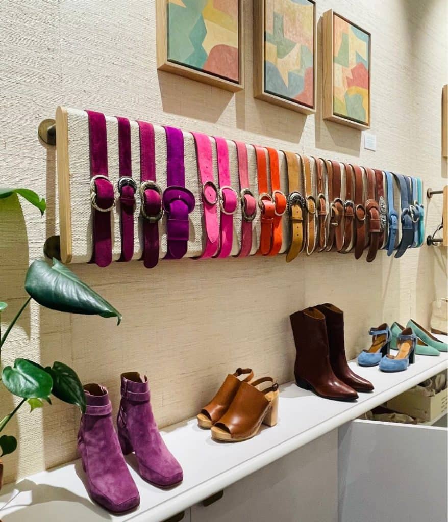A row of colorful belts on display at Sézane Paris. Several shoes and boots are also pictured just below.