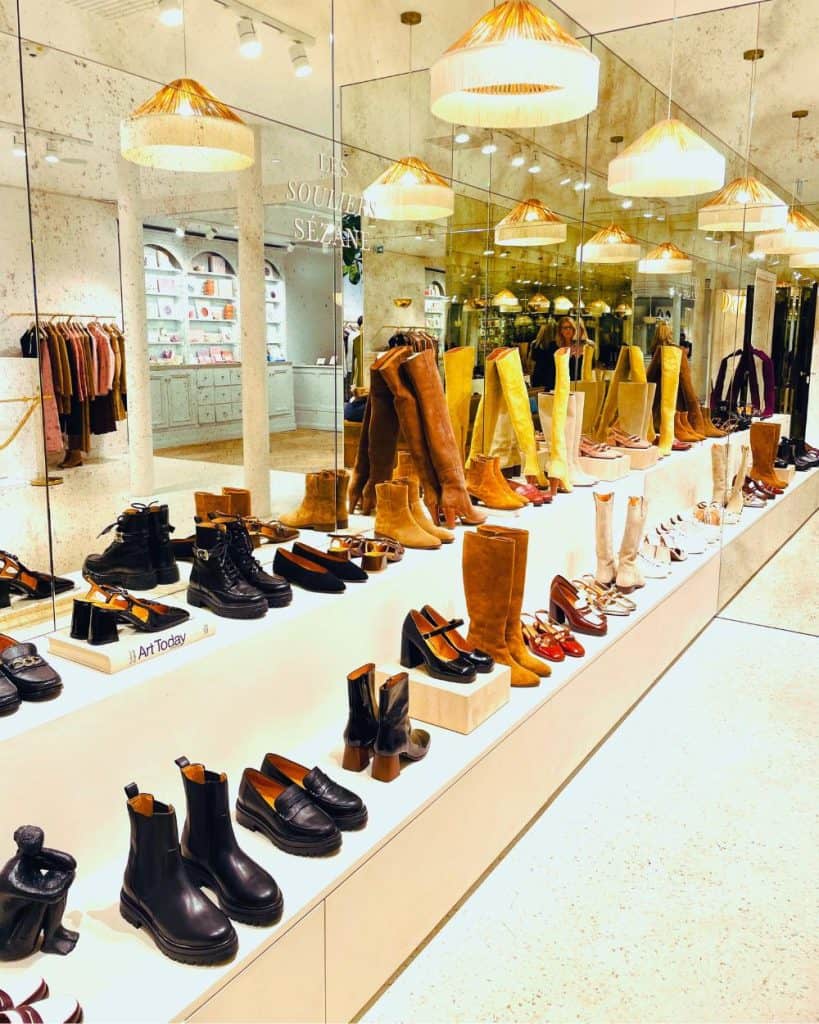 Inside the Sézane store in Le Marais, rows of shoes and boots are displayed in two tiers with mirrors behind. Colors are mostly browns and blacks as this is a fall shoe collection.