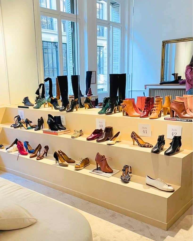 An array of shoes and boots are pictured on three levels of display, in front of a mirror at the Sézane Archives store in Paris.