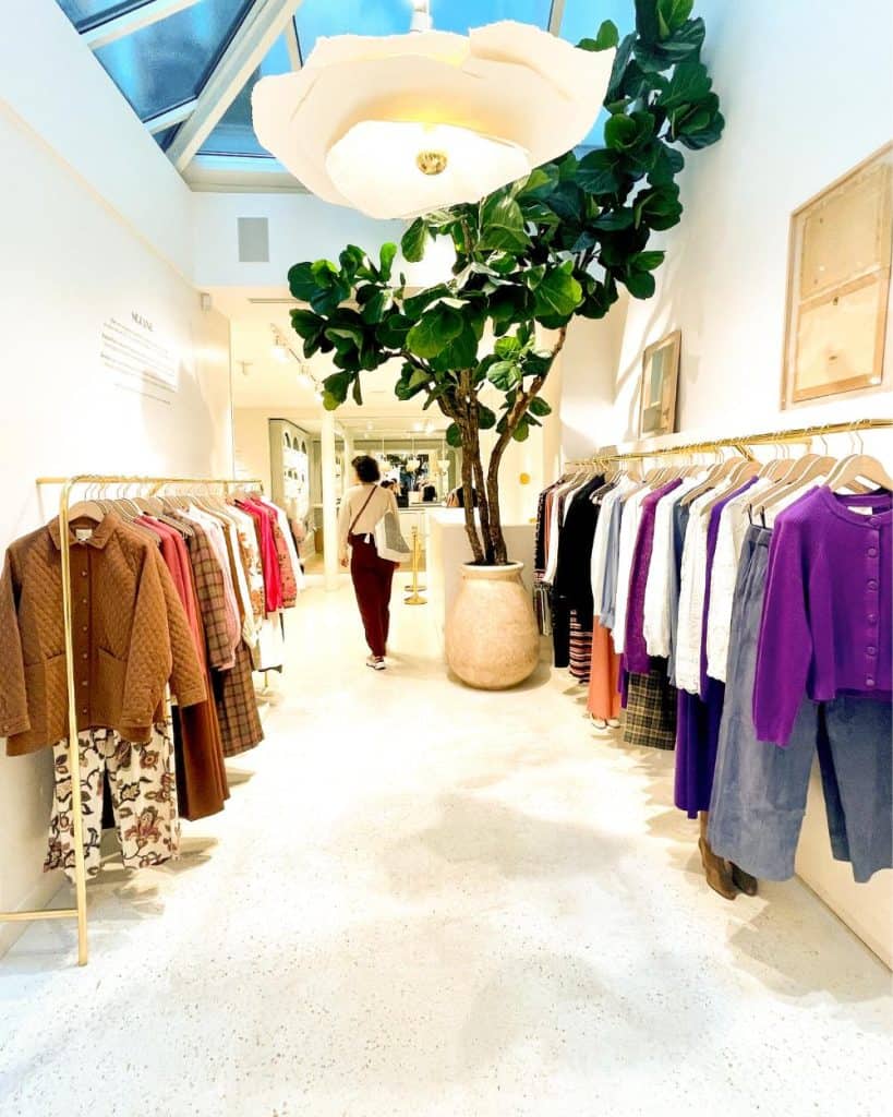 Sézane store in Paris's Le Marais. An open airy interior in shades of cream with clothing hanging on both sides and a large flower-shaped light fixture hanging from the ceiling.
