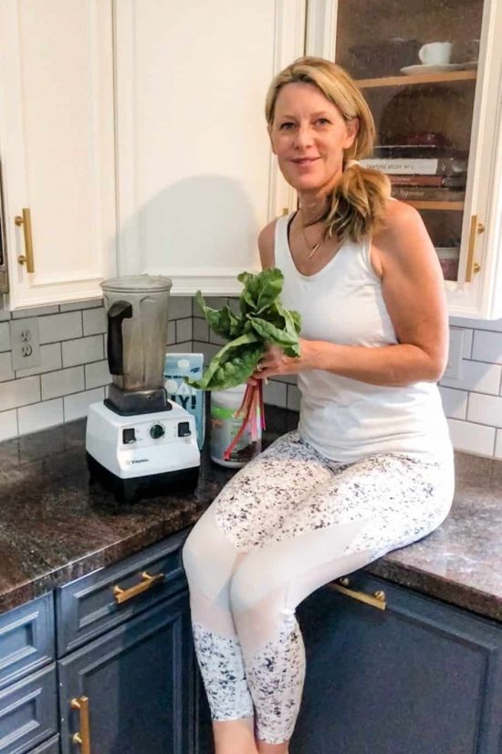 Susan Heinrich sits in her kitchen holding a handful of leafy greens
