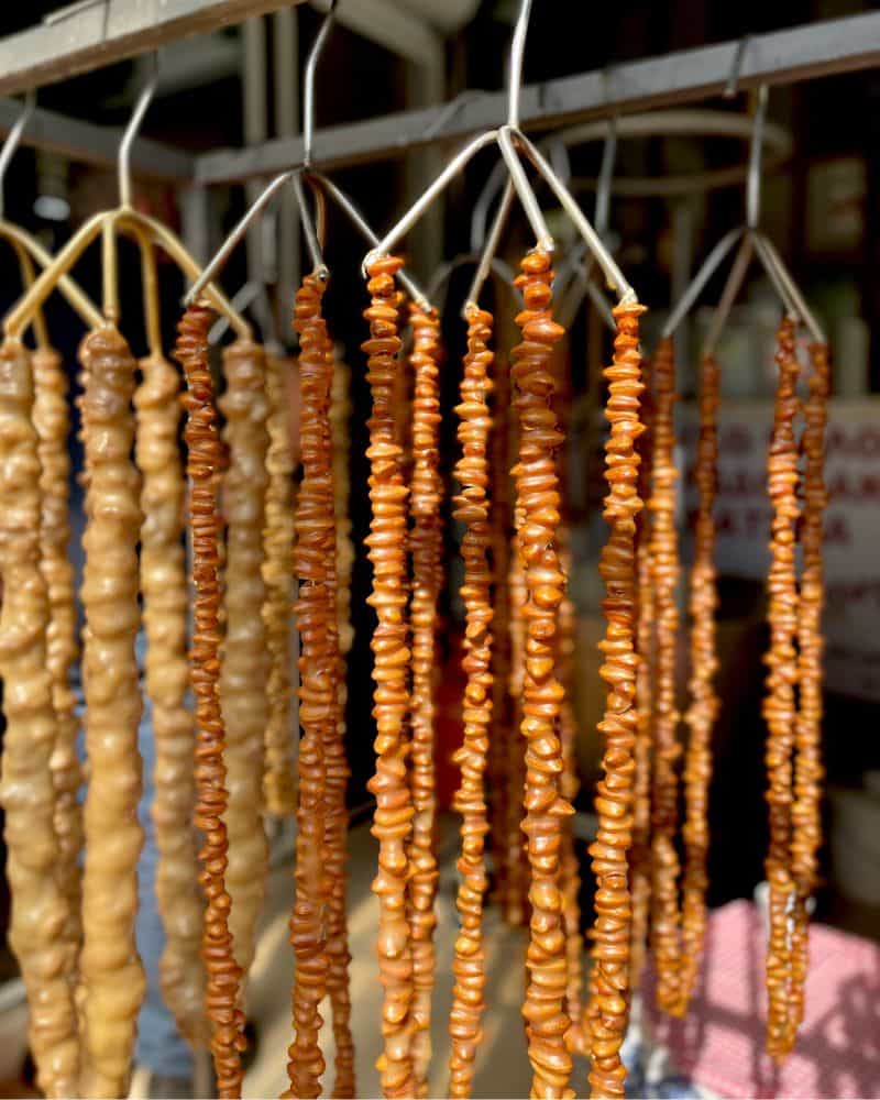 More than a dozen strands of golden brown shoushoukos hang drying in the sun. They are made of threaded rows of almonds coated in cooked syrup and left to dry.