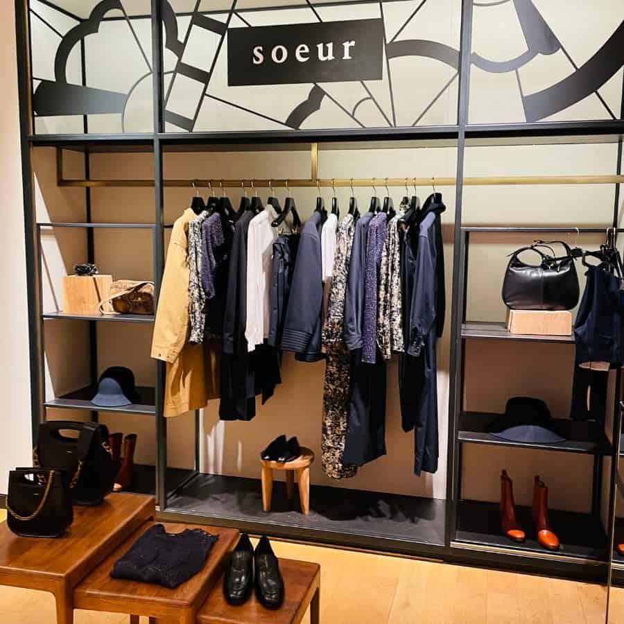 A rack of stylish clothes by Soeur amidst shelves with shoes and bags. Soeur is an affordable French clothing brand from Paris.